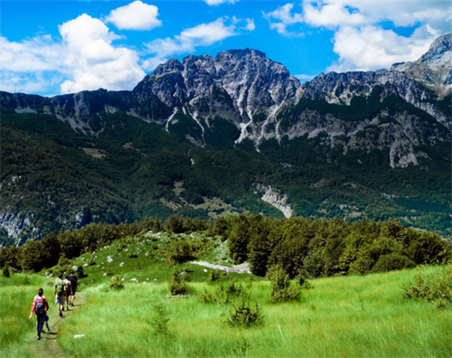 Group of hikers trekking on a grassy trail in the Accursed Mountains, Northern Albania