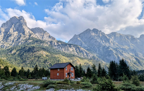 Traditional wooden mountain hut in the Valbona Valley, Accursed Mountains, Northern Albania, surrounded by pine trees and towering peaks