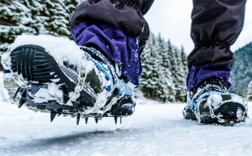 Close-up of boot-mounted microspikes providing traction on snowy trails during spring hikin