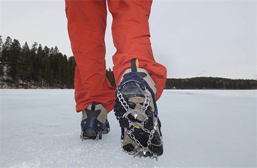  Hiker wearing chain-style microspikes walking on flat, frozen lake ice in winter conditions