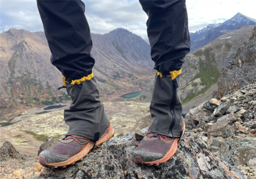 Mid-height hiking gaiters worn with trail shoes on alpine scree terrain, blocking rocks and dust