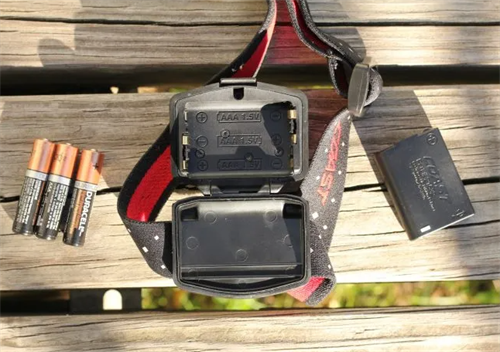 Headlamp battery compartment showing options for disposable AAA alkaline batteries vs. rechargeable battery packs