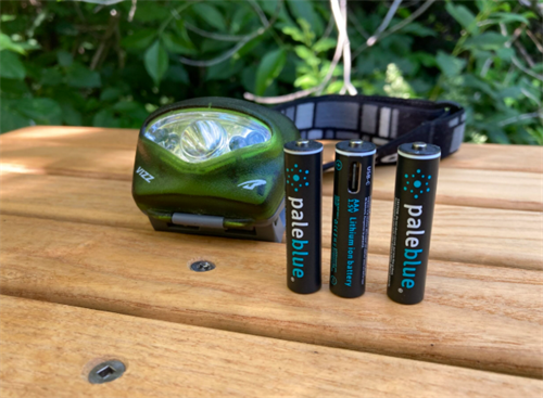 Green headlamp next to reusable Pale Blue lithium-ion rechargeable AAA batteries, for outdoor gear like GPS and headlamps