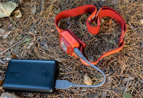 Red headlamp being charged via USB from an Anker power bank, demonstrating USB-rechargeable headlamp setup for trekking