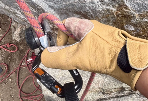 Leather climbing glove handling a belay device and carabiner, showing durable grip and protection for technical climbing