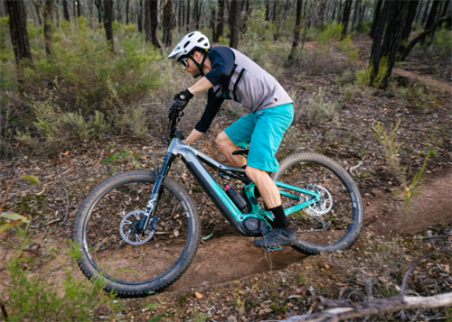 Male cyclist riding a full-suspension electric mountain bike through a forest trail, showcasing e-bike use on singletrack