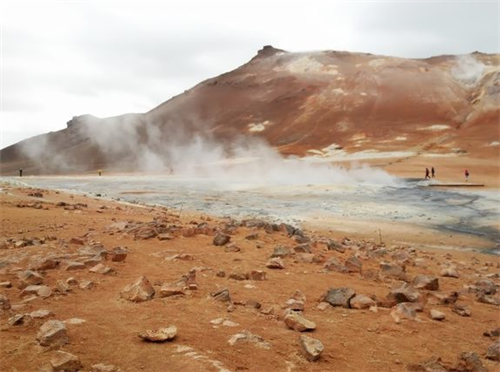 Steam rising from geothermal vents in a barren, rust-colored volcanic landscape, resembling a Martian hiking destination on Earth