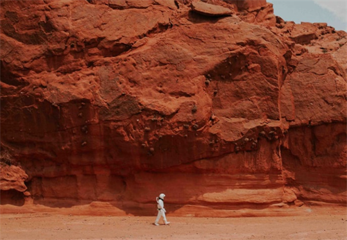 Solo hiker in a white suit walking beneath towering red rock formations, capturing the alien aesthetic of Mars-inspired hiking trails