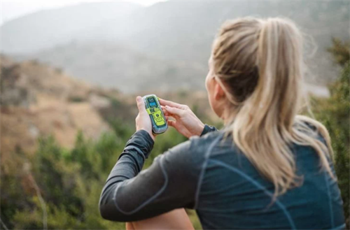 Hiker activating a personal locator beacon, a type of wearable safety tech, as an alternative to traditional guide support