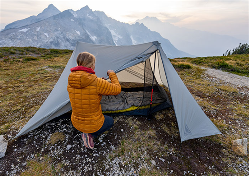 Hiker setting up a sub-2-pound ultralight tent on an alpine ridge, showcasing lightweight, high-tech camping gear