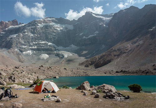 Wild camping by a turquoise lake in Tajikistan’s Fann Mountains, surrounded by snow-covered peaks