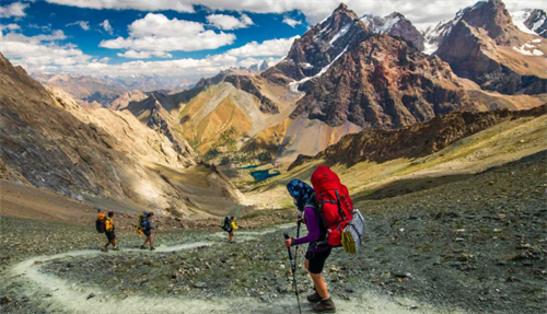 Group of trekkers hiking a rocky trail through Tajikistan’s Fann Mountains, with snow-capped peaks and alpine lakes in the background