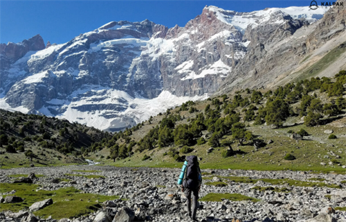 Solo hiker trekking through a rocky riverbed toward snow-capped peaks in Tajikistan’s Fann Mountains