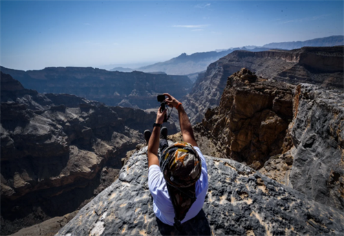 Hiker taking photos from a dramatic cliff edge in Oman’s Hajar Mountains canyons