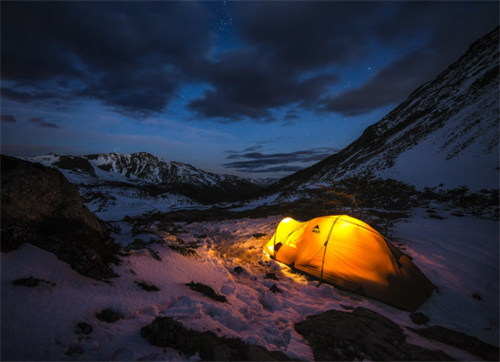Glowing tent lit up at night in a snowy mountain valley, wild camping on the Dientes de Navarino Circuit, Chile