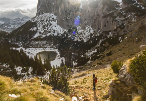 Solo hiker descending a trail toward a frozen alpine lake in Durmitor National Park, Montenegro
