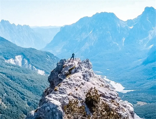 Hiker standing on a rocky outcrop overlooking the Valbona Valley and Albanian Alps on the Valbona–Theth hiking trail